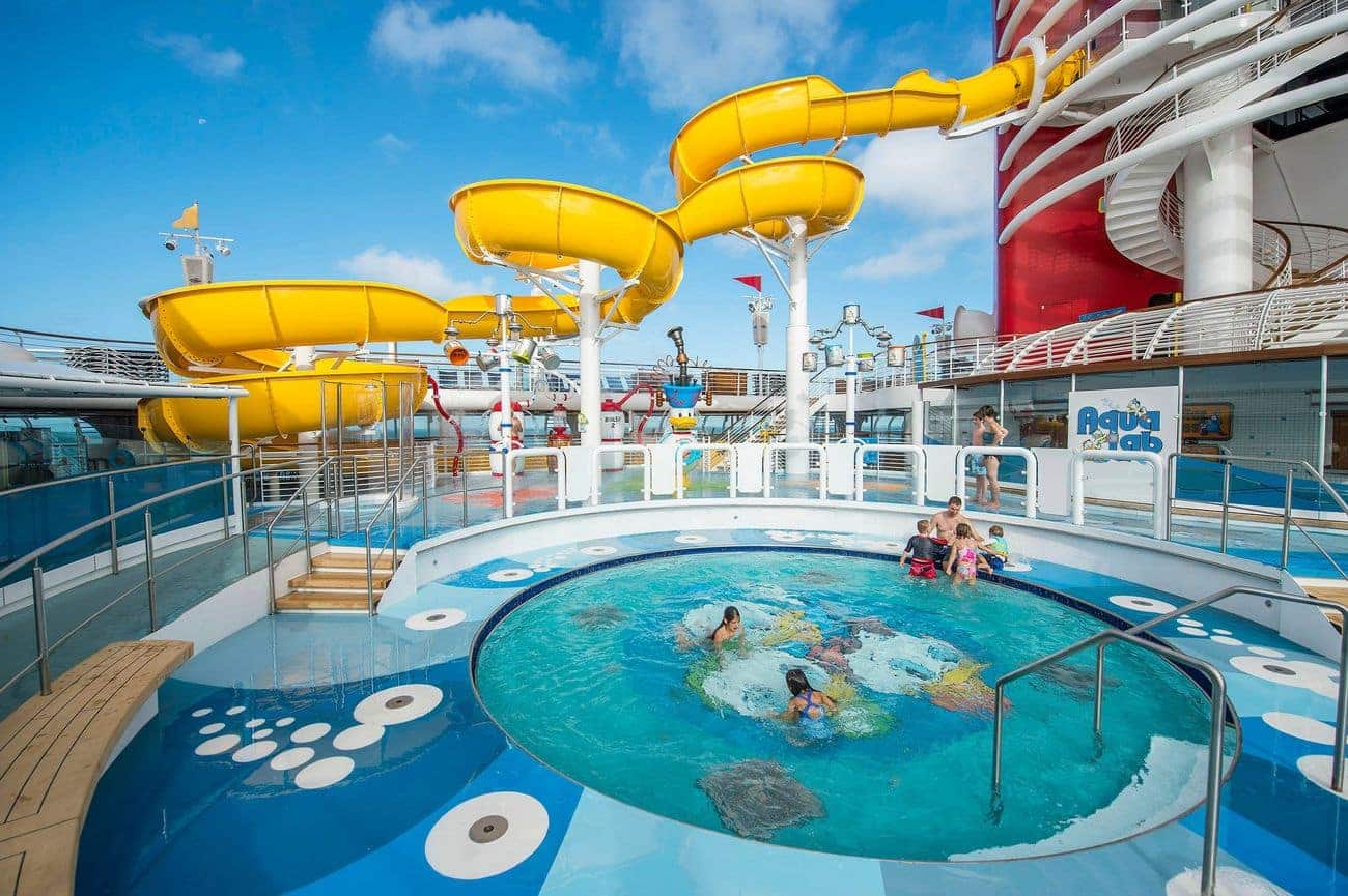 Families enjoying the AquaLab water play area on Disney Wonder with twisting yellow slides and bubbling splash zones
