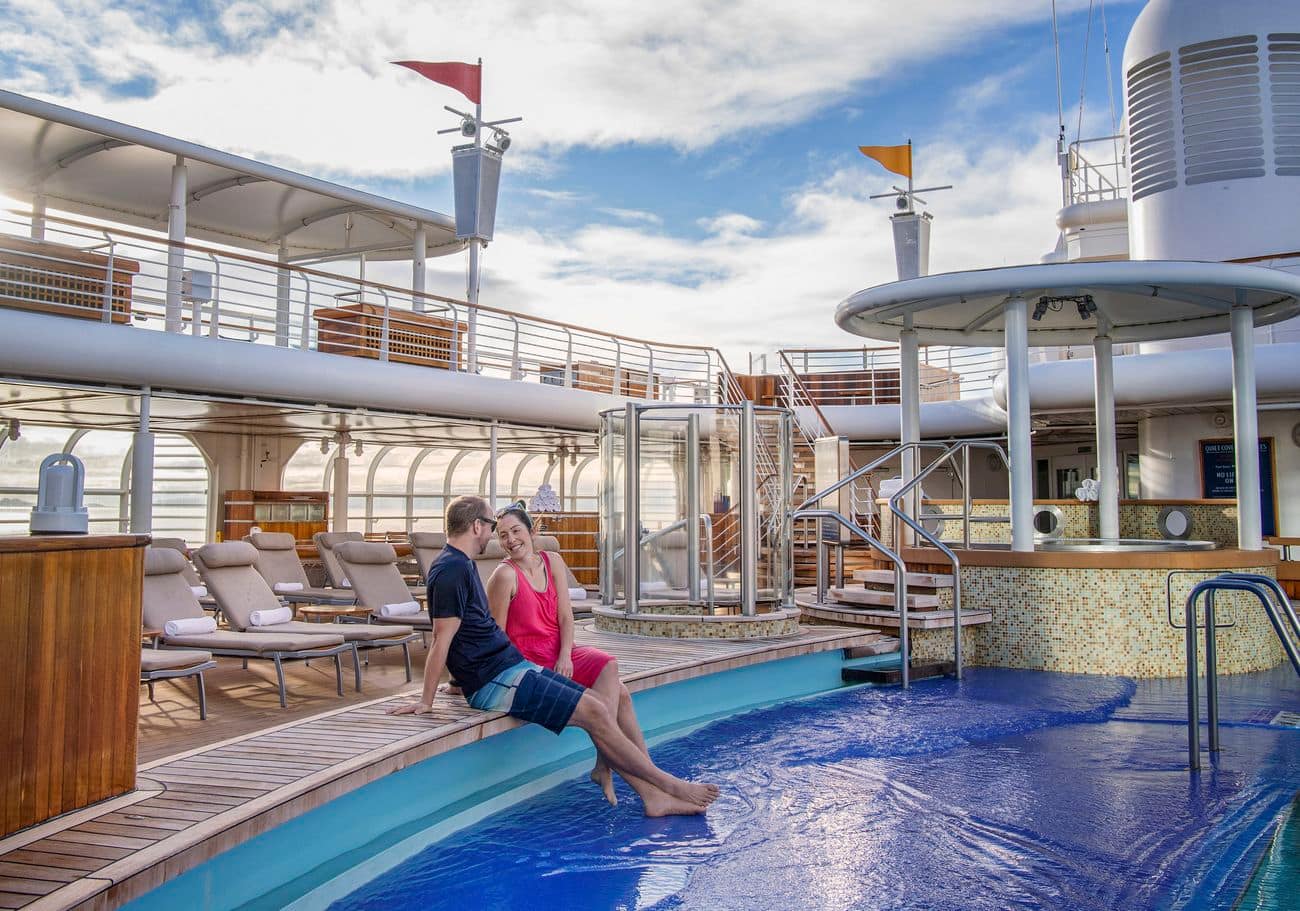 An adult couple relaxing by the Quiet Cove pool surrounded by loungers and open-air views