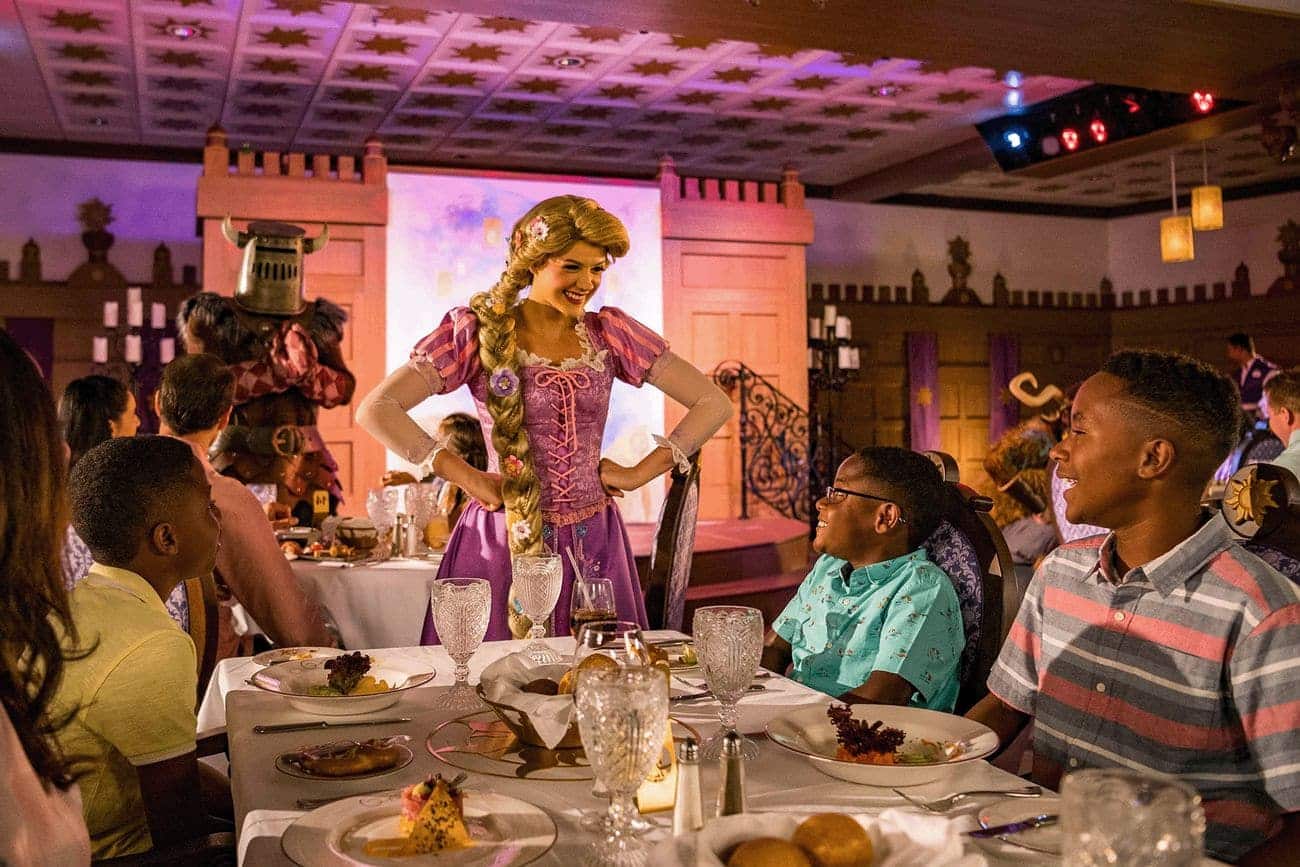 Rapunzel greeting guests at Rapunzel’s Royal Table aboard Disney Magic inside a warmly lit dining room with castle themed décor