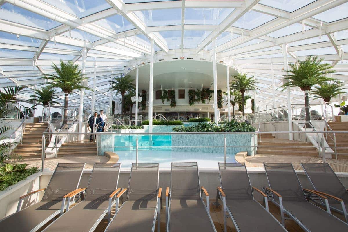 Indoor Solarium pool area with glass roof and tropical décor on Royal Caribbean’s Quantum of the Seas