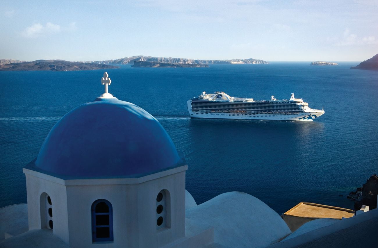 Emerald Princess sailing past Thira in Santorini, Greece, with blue-domed church in foreground