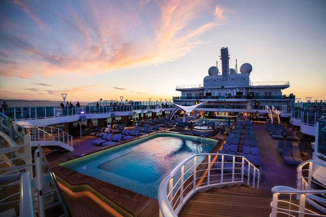Sky Princess sun deck featuring a central pool surrounded by loungers under a colorful sunset sky