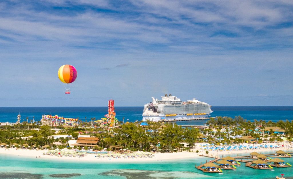 Aerial view of Coco Beach Club at Perfect Day at CocoCay with Symphony of the Seas docked nearby and the Up Up and Away balloon rising above the island
