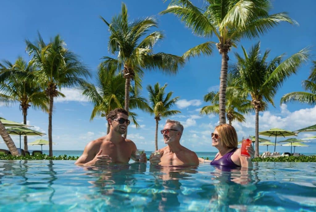 Guests relaxing in the infinity pool at Coco Beach Club with turquoise Bahamian waters and palm trees behind them