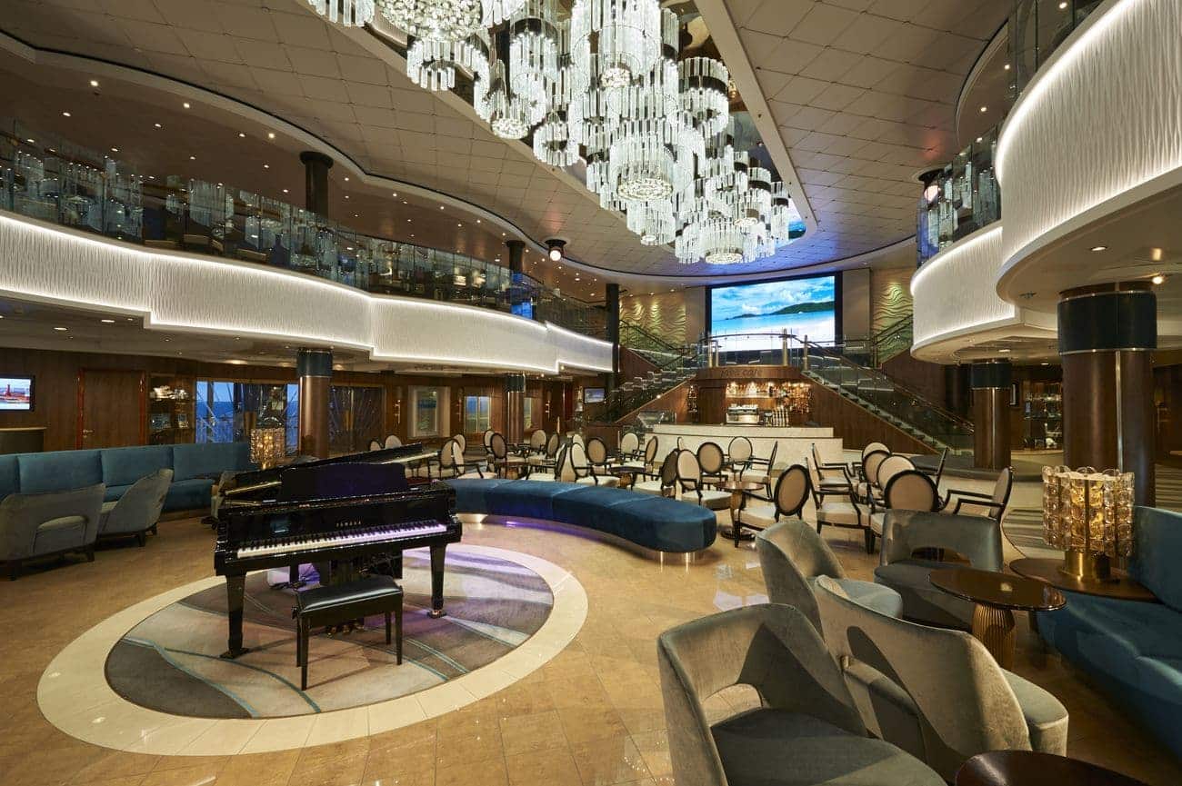Multi-level atrium aboard Norwegian Jade featuring a grand chandelier, piano lounge seating, and sweeping staircases