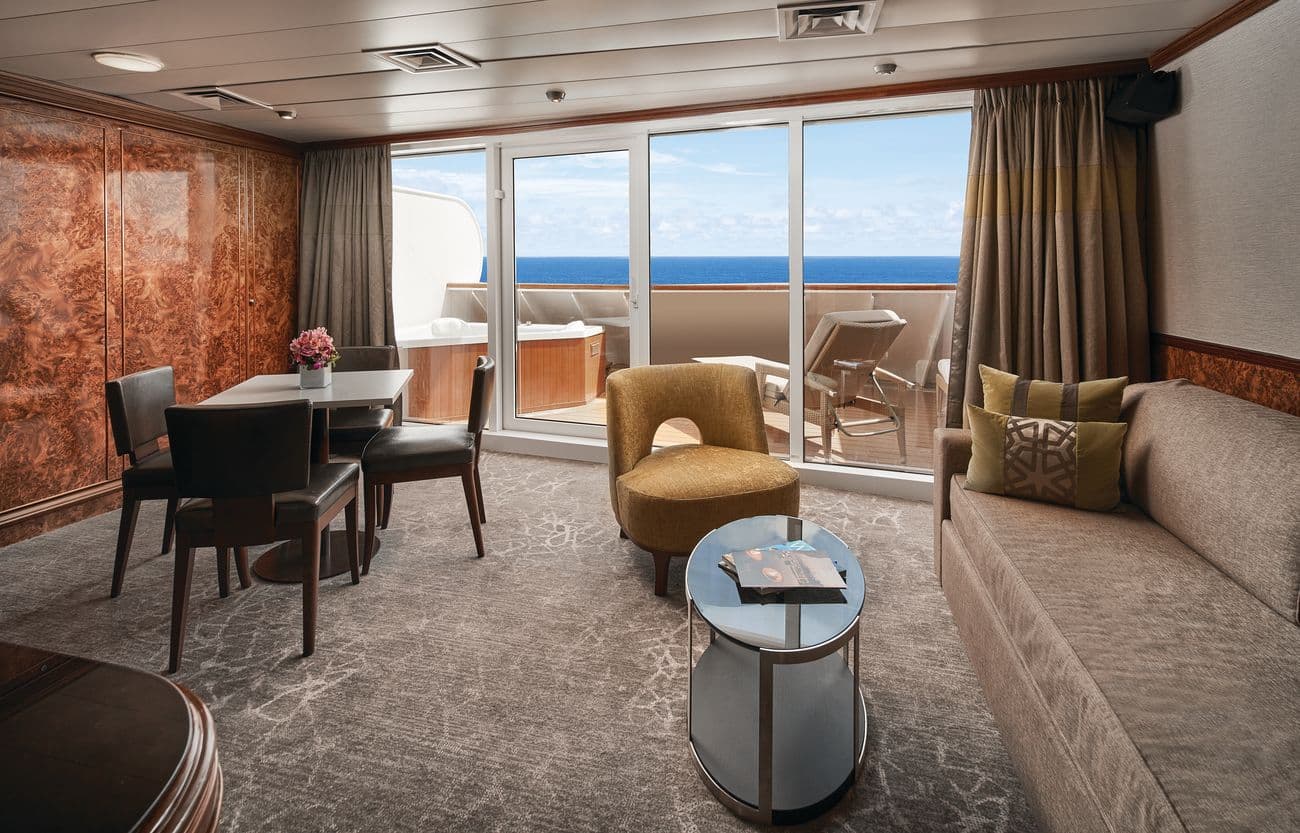 Owner’s Suite living area with dining table, sofa seating, and large private balcony overlooking the ocean