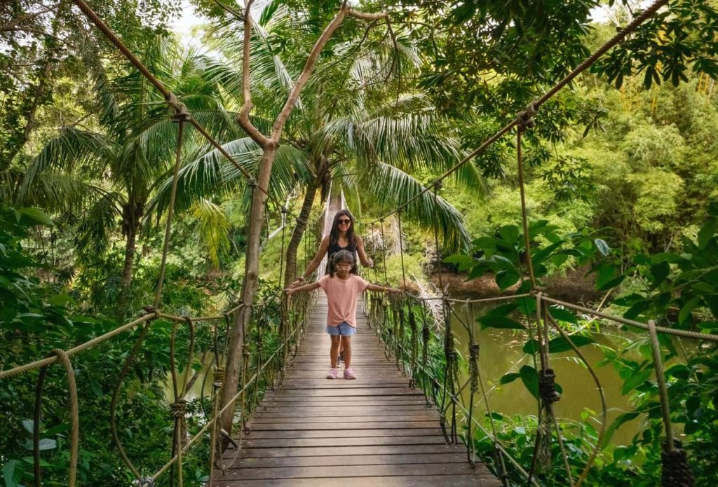 Mother and daughter walking across a rustic wooden suspension bridge in the lush jungle of Roatán Honduras
