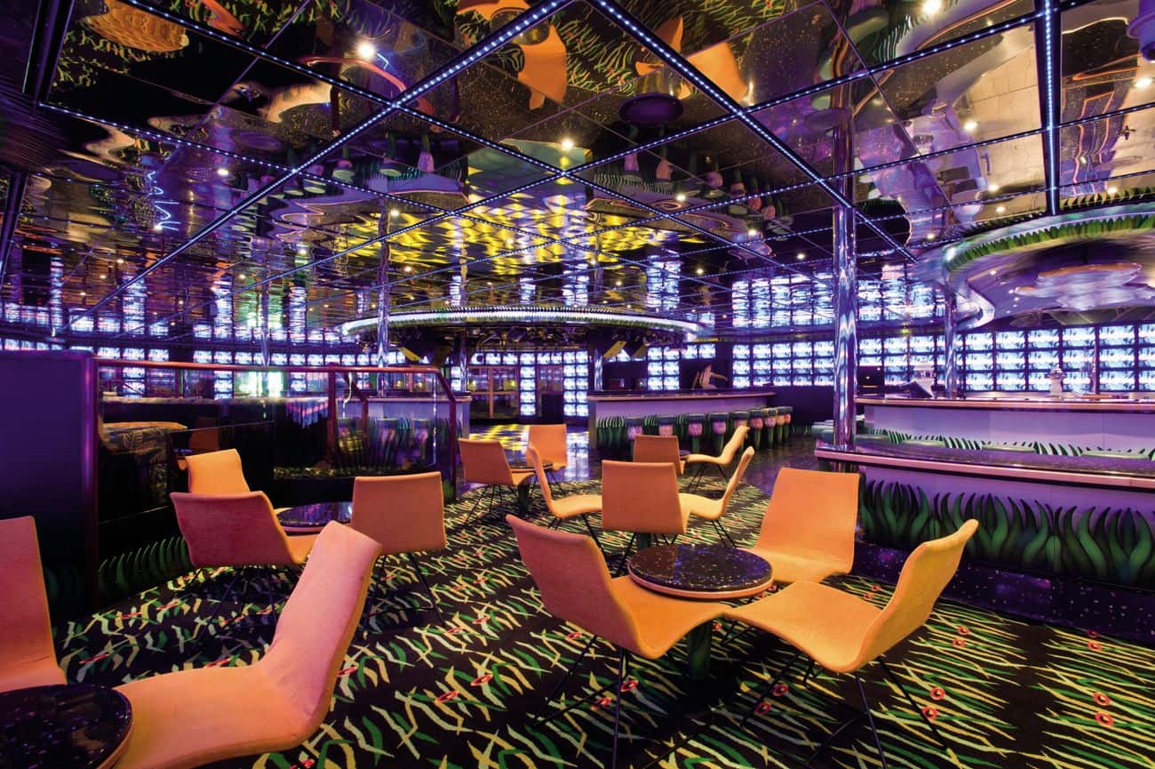 Neon-lit nightclub interior on Carnival Conquest with patterned carpet, reflective ceilings, and lounge seating surrounding the dance area