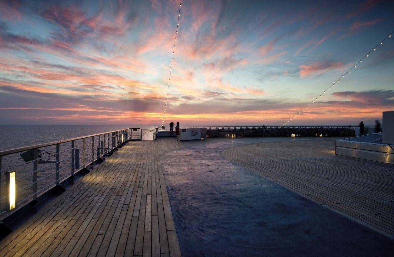 Open teak deck with whirlpool spa overlooking calm ocean waters during a colorful sunset at sea