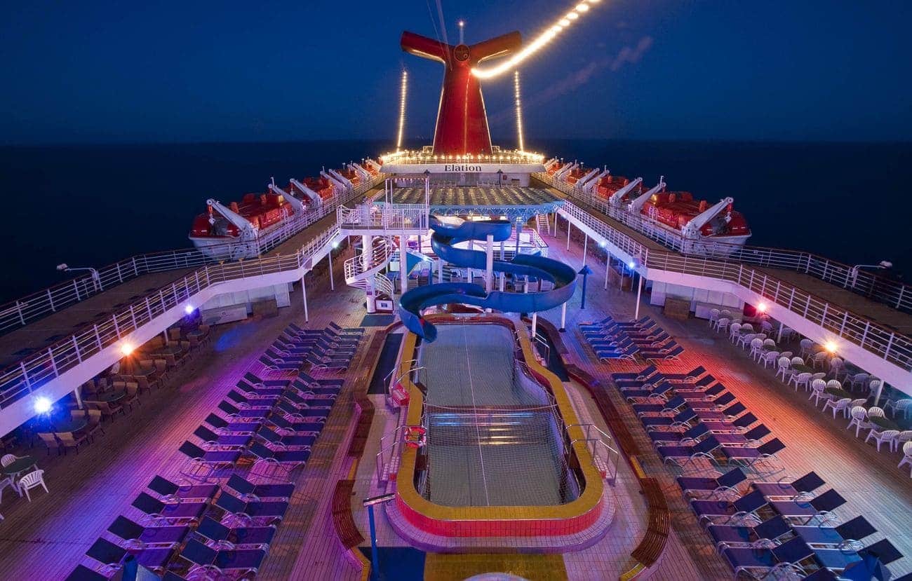 Lido deck pool and twisting waterslide illuminated at dusk