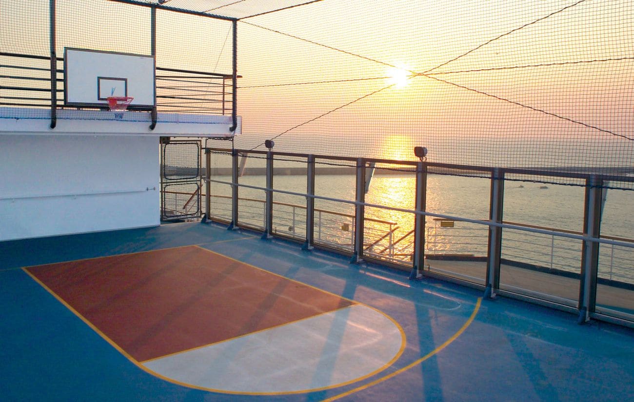Outdoor basketball court enclosed by safety netting overlooking the open ocean at sunset