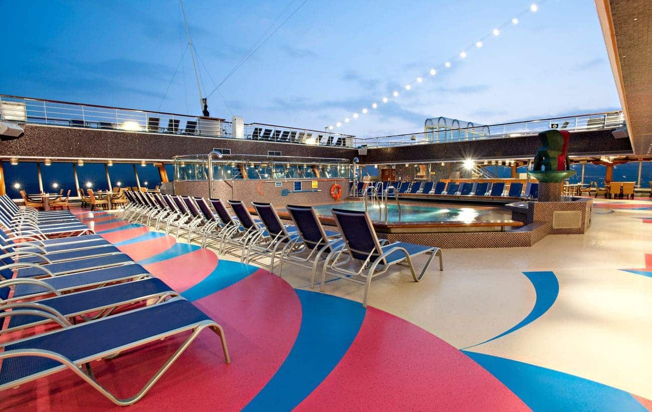 Lido deck pool area with rows of loungers and colorful flooring