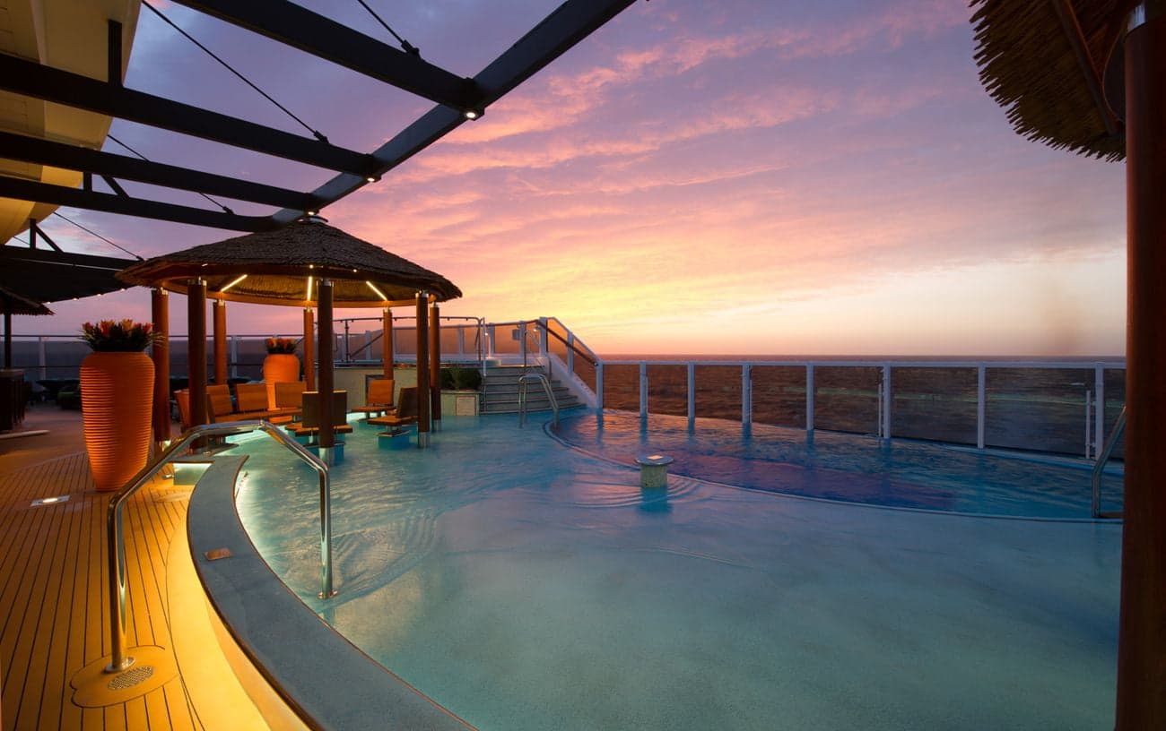 Havana Bar pool area at sunset with curved pool, shaded cabanas, and ocean views from the deck