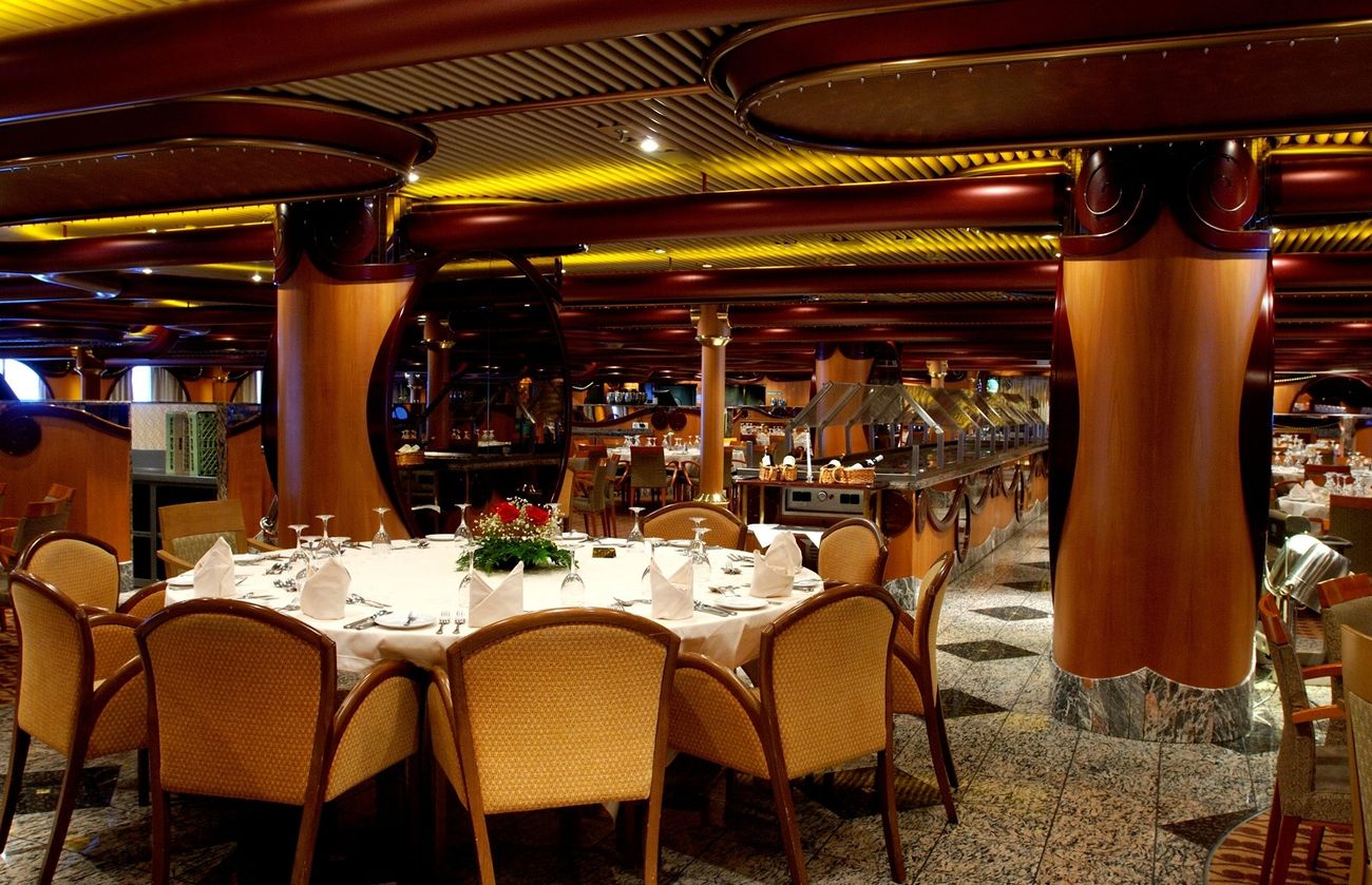 Carnival Paradise Destiny Dining Room with round tables and warm wood interiors