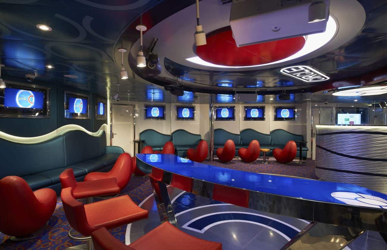 Carnival Sunshine Circle C teen lounge with curved blue seating, red chairs, and wall-mounted screens