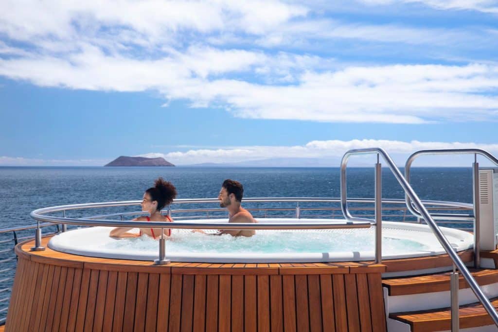 Guests relaxing in an ocean-view jacuzzi on the deck of an expedition ship while sailing past Galapagos islands