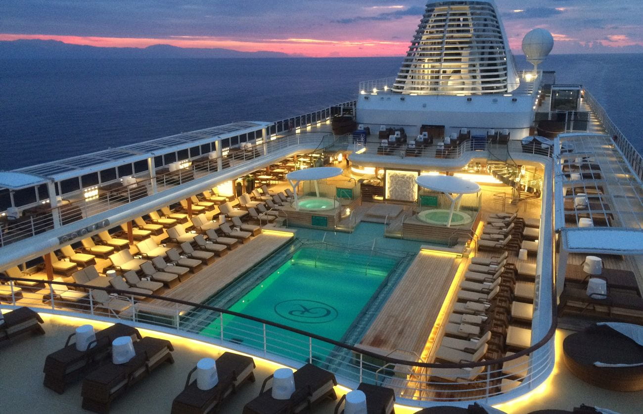 Seven Seas Explorer pool deck at sunset with illuminated swimming pool, whirlpools, and neatly arranged loungers