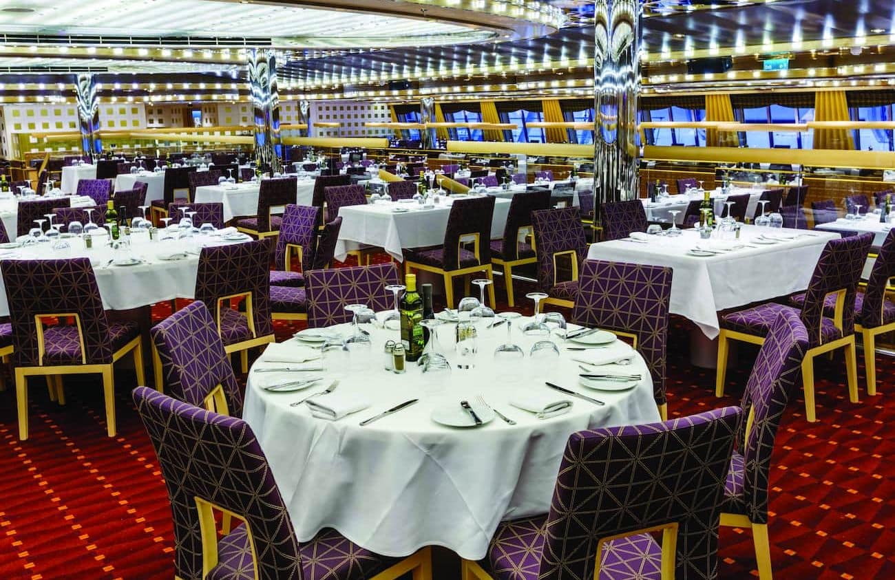 Adularia Restaurant dining room with white table settings, mirrored columns, and patterned purple chairs.