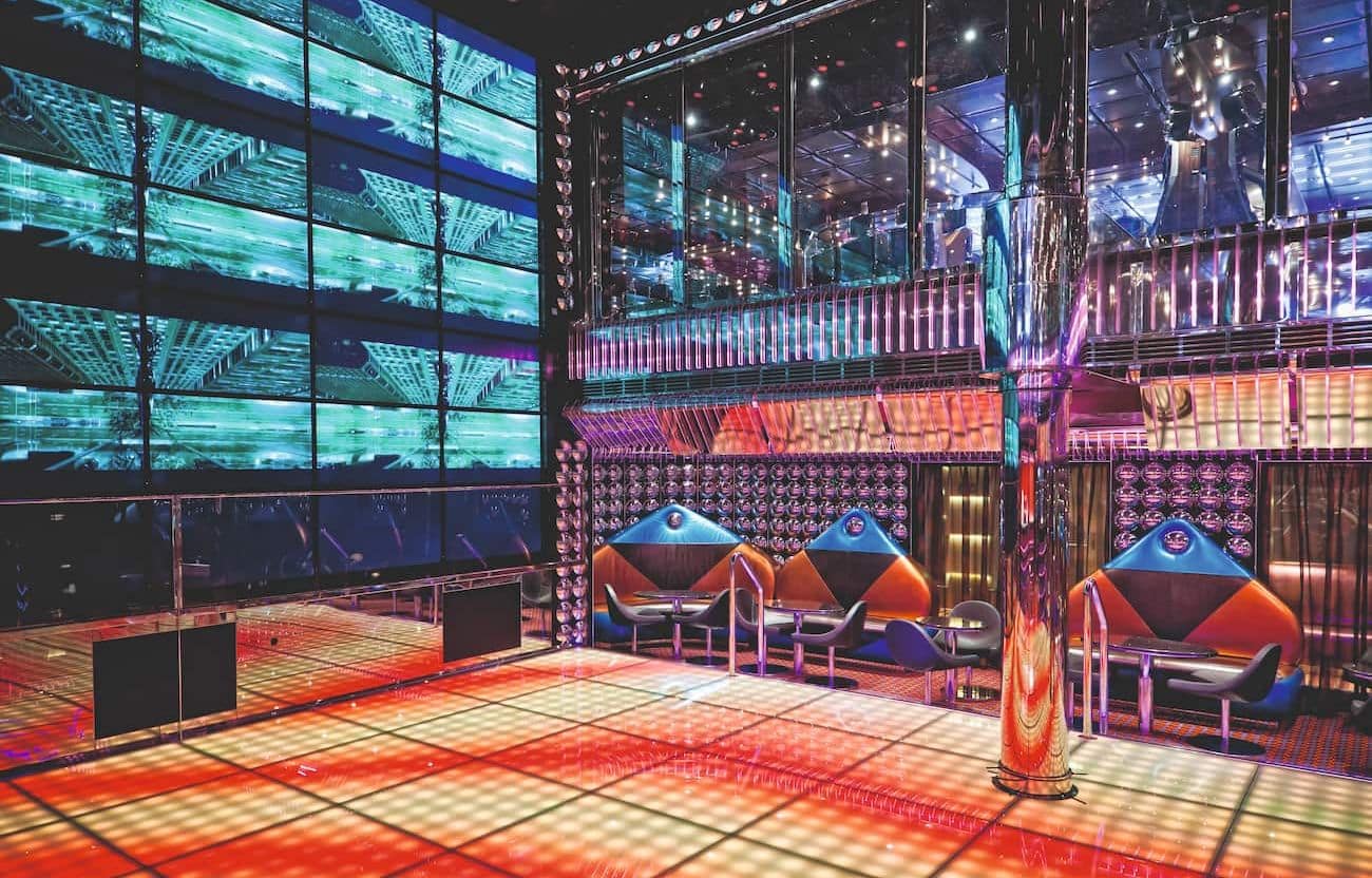 Babylon Discoteque with an illuminated dance floor, mirrored columns, video wall, and colorful neon lighting.
