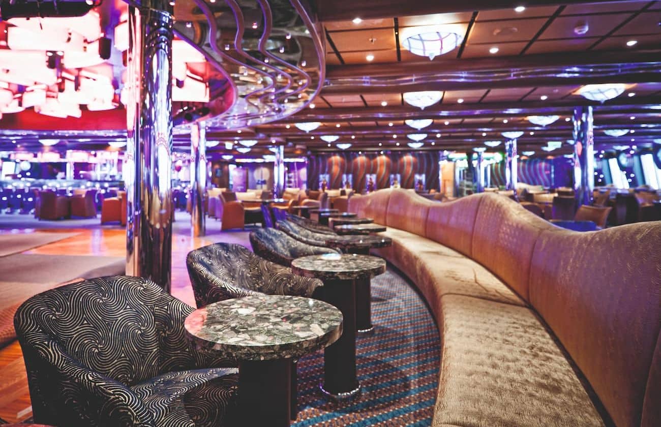 Grand Bar Topkapi lounge with curved banquettes, marble-topped tables, chrome columns, and purple ambient lighting.
