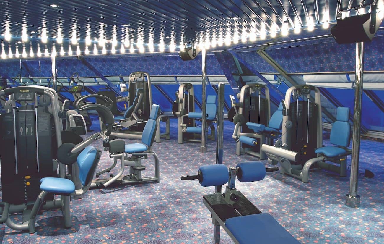 Club Salute Saturnia 1927 fitness center with strength machines, blue seating, and forward-facing windows.