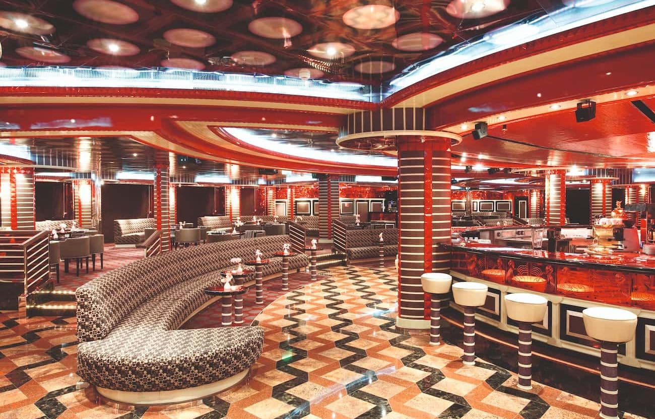 Around the Clock Lounge with curved banquette seating, glossy striped columns, and an illuminated bar area
