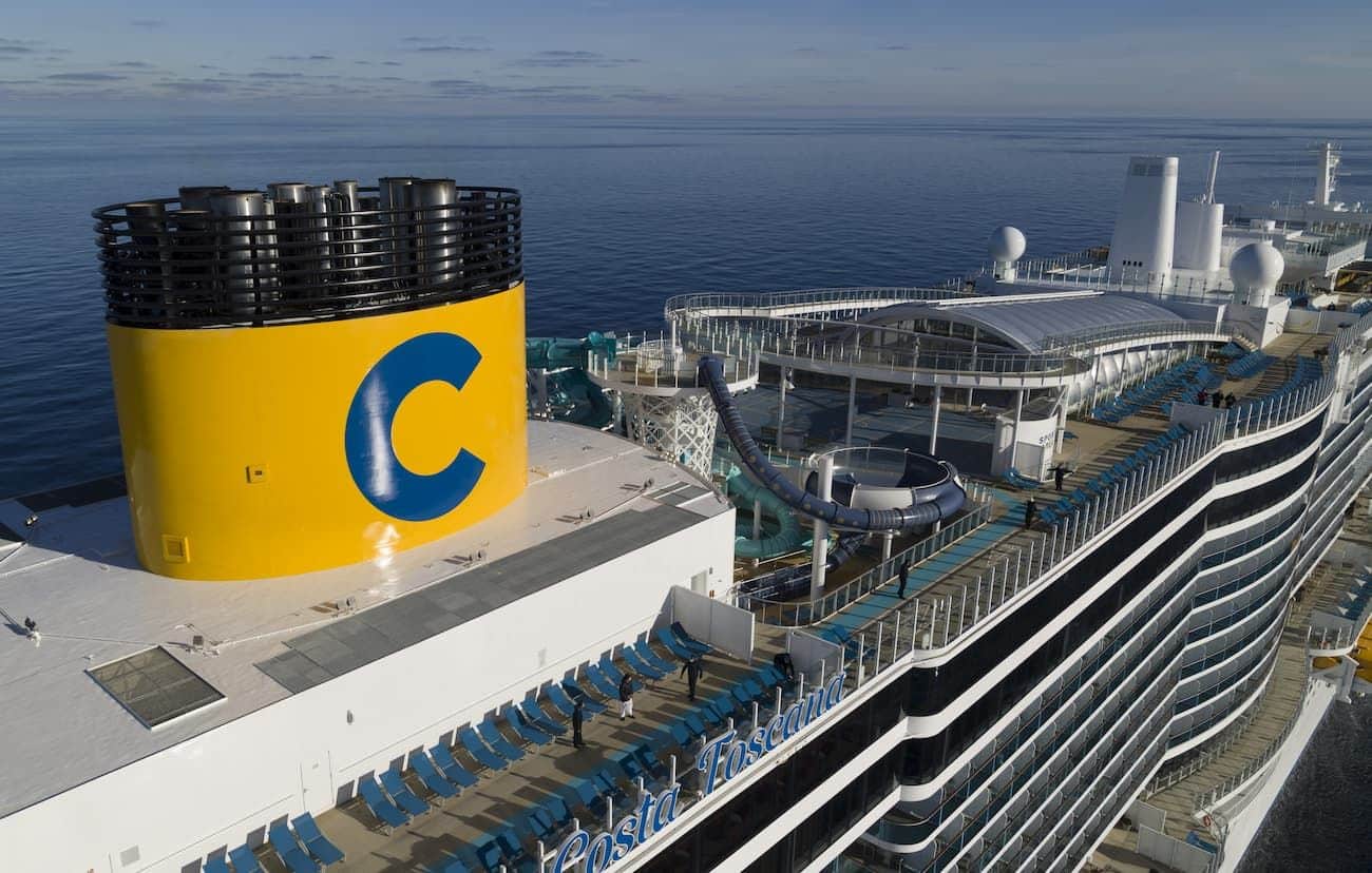 Costa Toscana Open Deck aerial view with the yellow funnel, waterslides, sun loungers, and upper-deck spaces beside a calm sea.