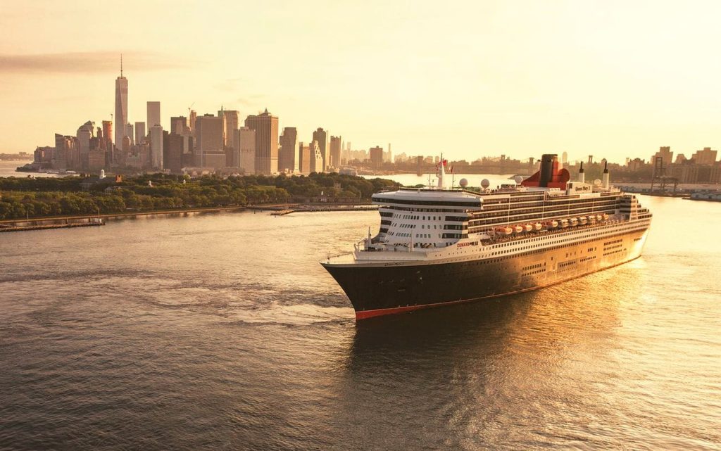 Queen Mary 2 sailing in New York Harbor at sunset with the Lower Manhattan skyline in the background