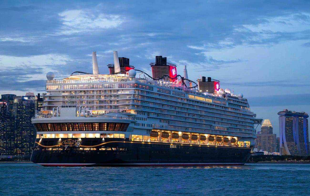 Disney Adventure sailing past the Singapore skyline at dusk, with Marina Bay Sands visible in the background