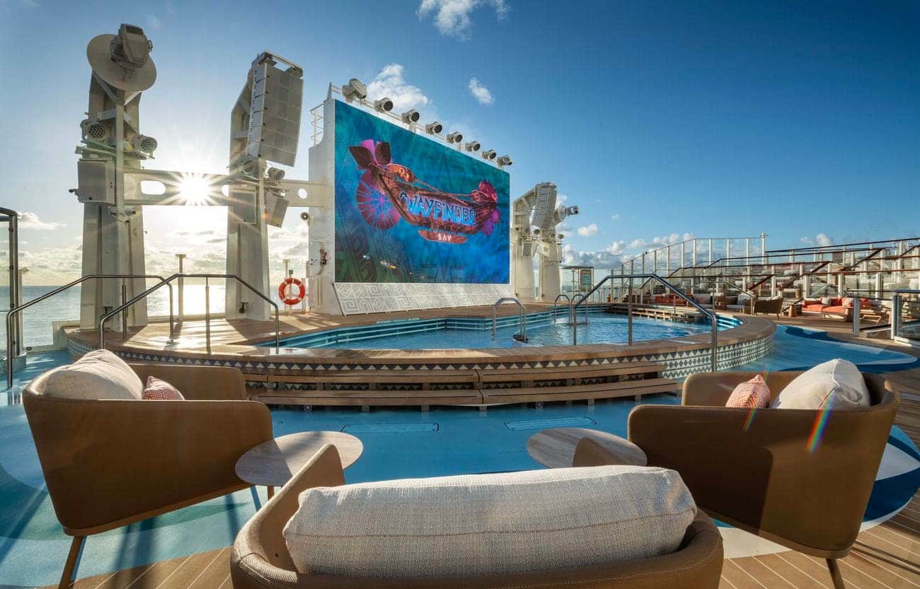 Wayfinder Bay pool deck on Disney Adventure, featuring a giant outdoor screen, sunlit loungers, and ocean views
