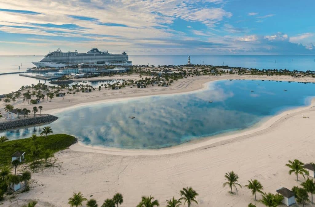 Aerial view of Ocean Cay with a calm lagoon, pale sand beaches, palm-lined shores, and MSC Seashore docked nearby beneath a wide blue sky