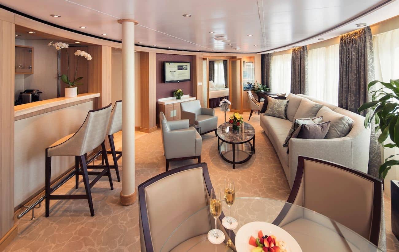 Owner’s Suite living area with dining table, bar seating, sofa, and large windows