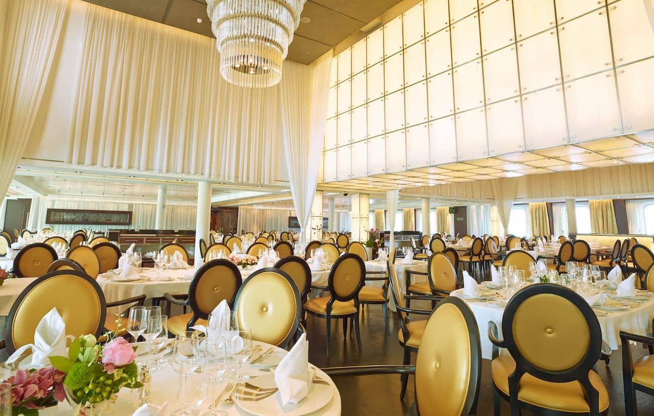 Seabourn Quest The Restaurant dining room with formal table settings, chandelier lighting, and cream curtains
