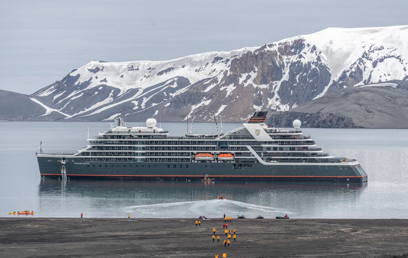 Seabourn Venture anchored off Deception Island, Antarctica with guests landing below snowy volcanic slopes