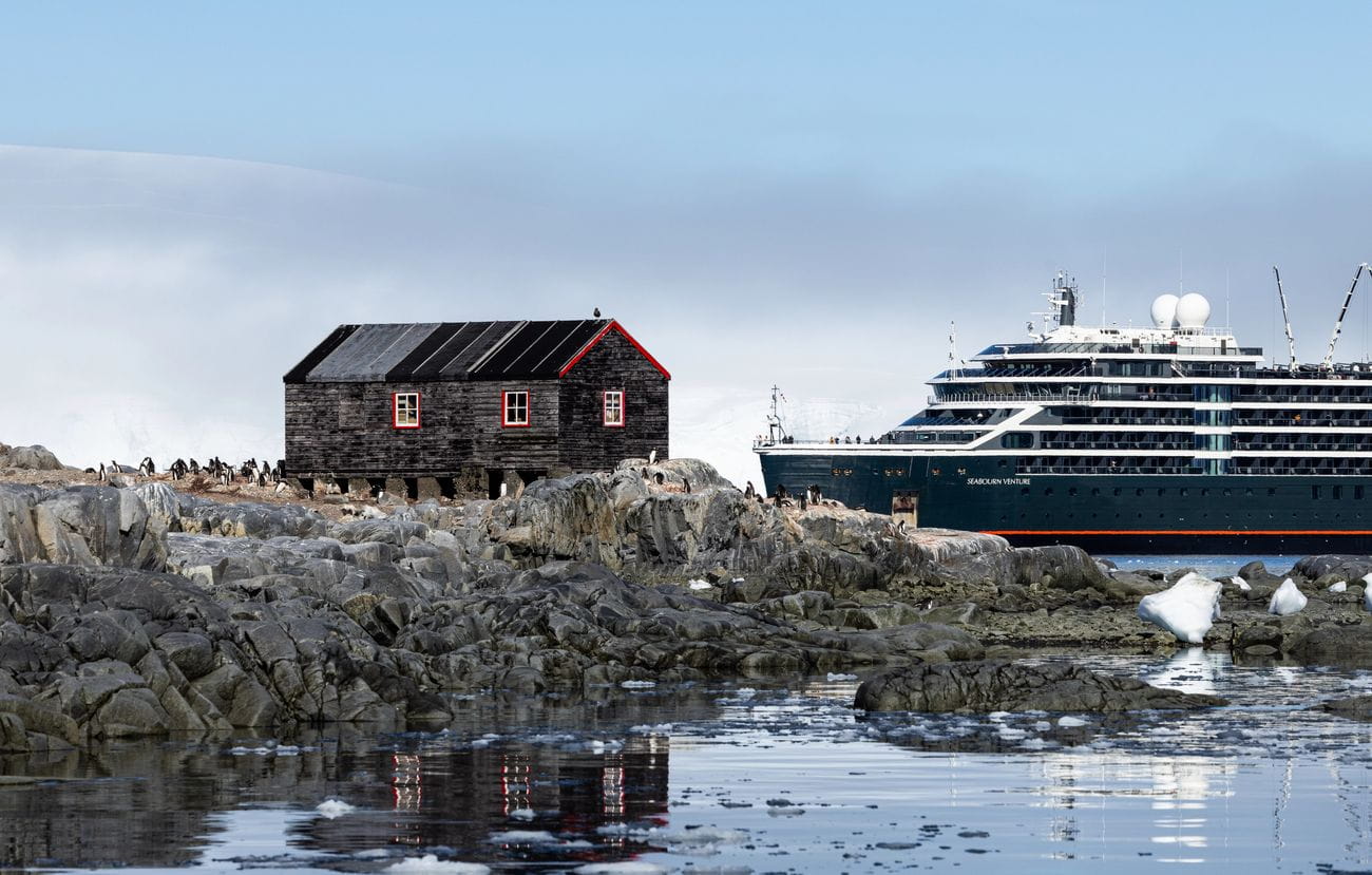 Seabourn Venture beside Port Lockroy in Antarctica with penguins and the historic black building ashore