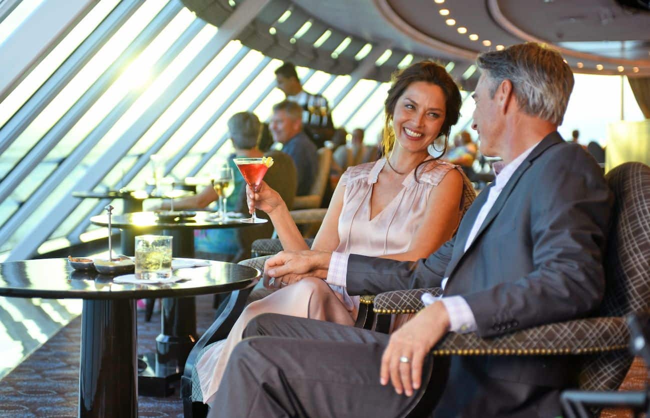 Couple enjoying drinks in Horizons Bar beside panoramic windows at sunset