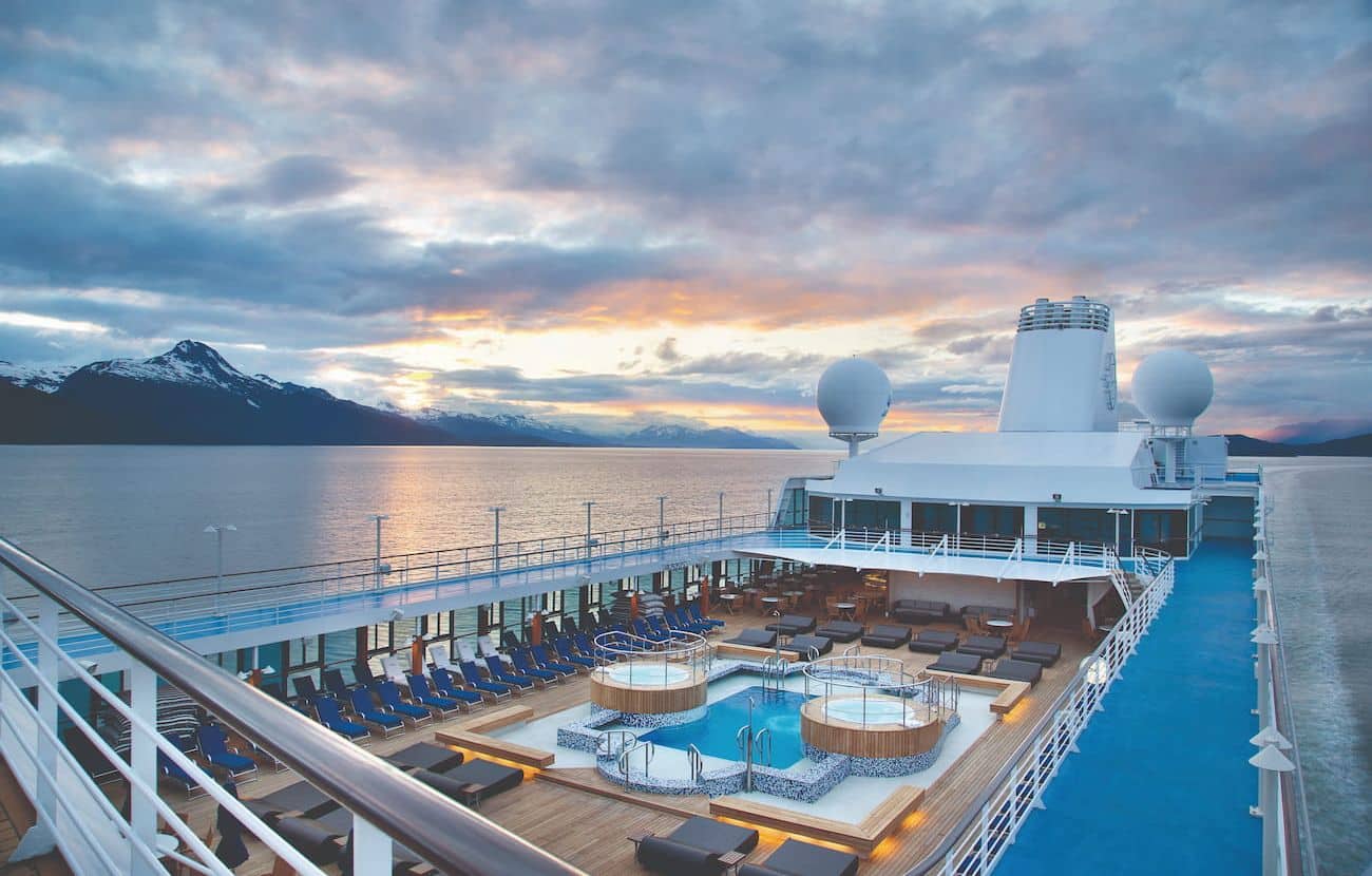 Oceania Nautica Pool Deck at sunset with loungers, whirlpools and mountain views