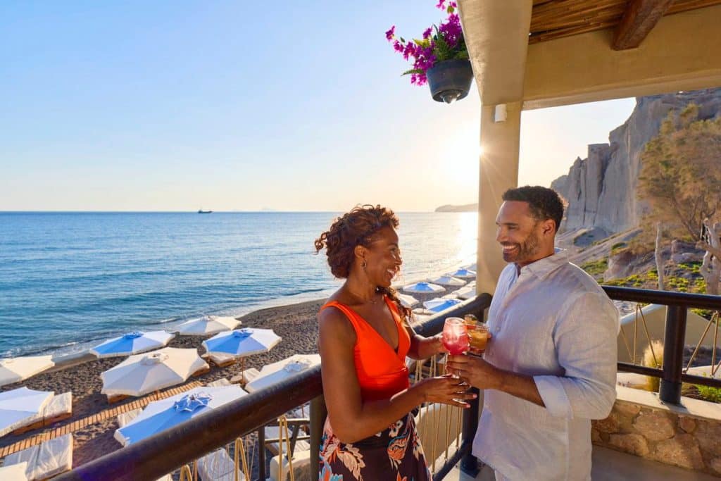 Couple enjoying drinks on a Santorini terrace above the black-sand beach