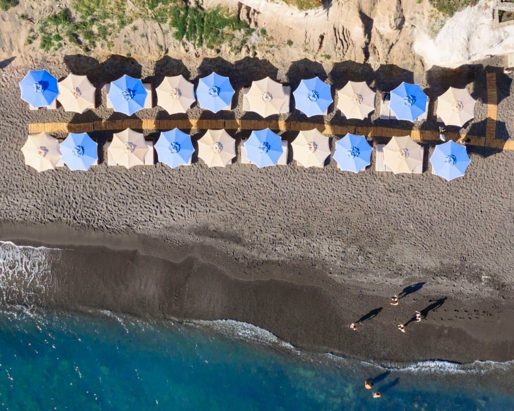 Aerial view of blue and white umbrellas arranged on Santorini black sand