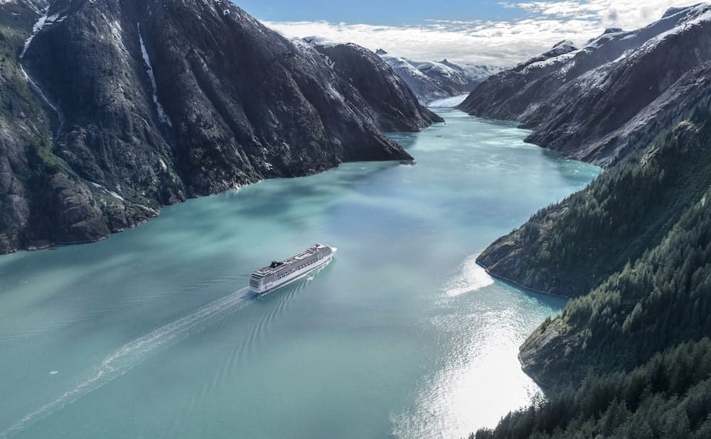 MSC Poesia Alaska sailings through a turquoise fjord surrounded by steep forested mountains
