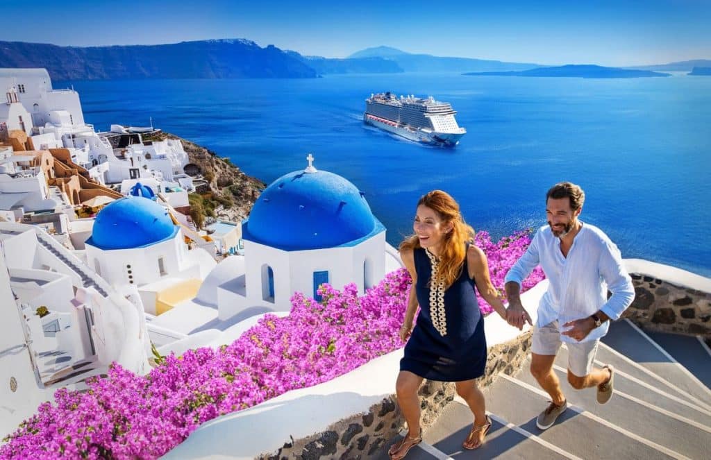 Mediterranean cruises in 2026: Couple walking through Oia, Santorini with Norwegian Escape offshore
