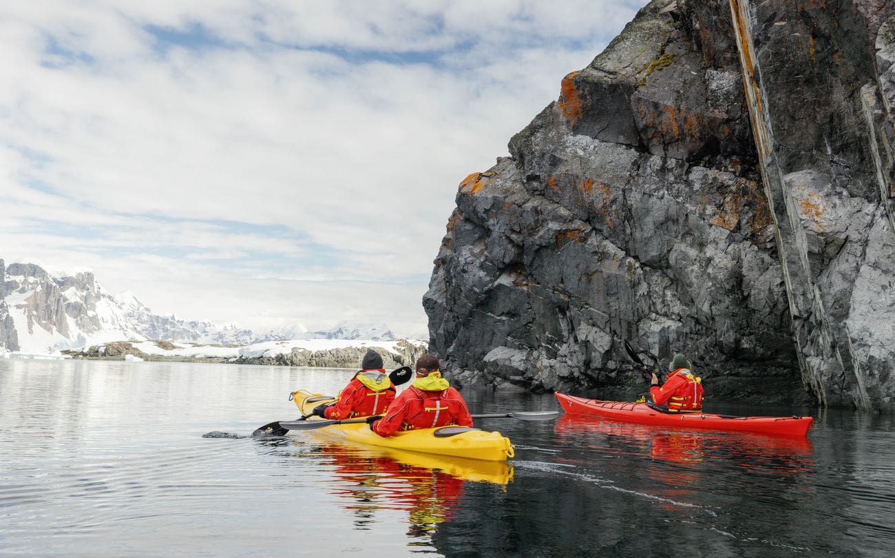 Expedition guests kayaking beside rocky cliffs near Pleneau and Winter Island in Antarctica