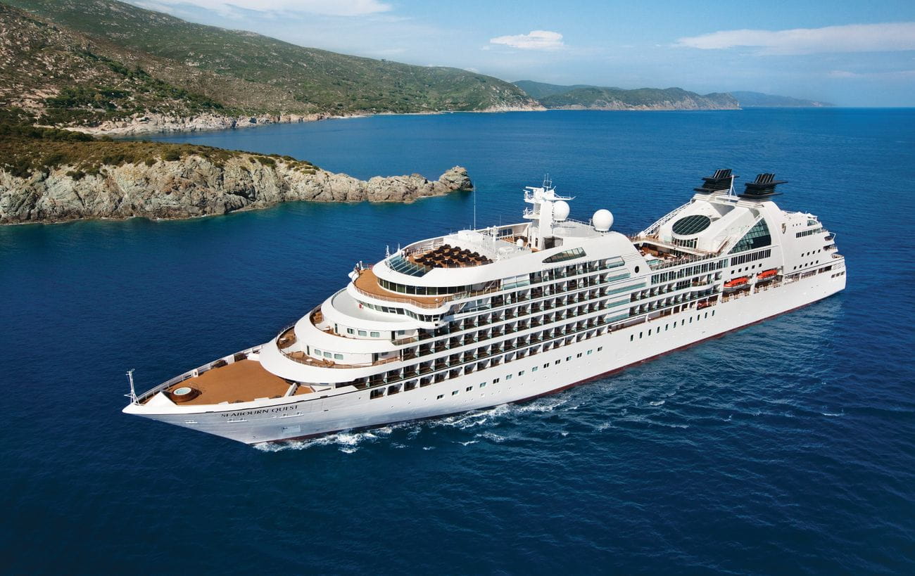 Seabourn Quest cruising through deep blue water near a rugged coastline