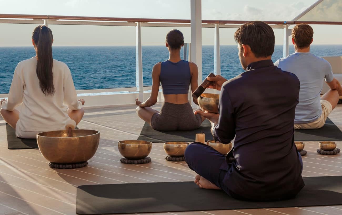 Guests practicing sunrise yoga with singing bowls on an open ocean-facing deck